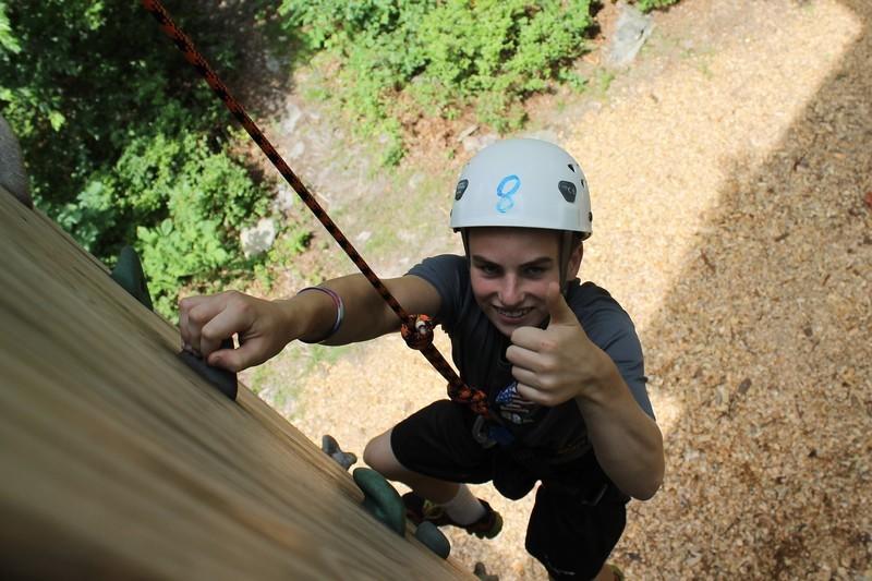 Scout climbing up the rock wall, giving a thumbs up